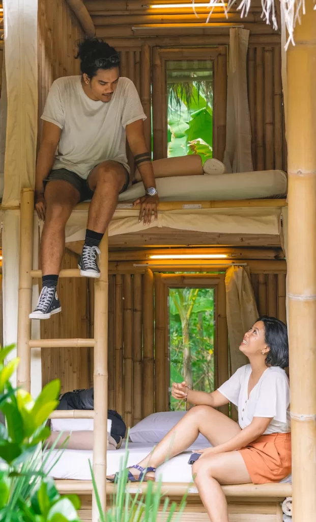 man in white shirt and brown shorts sitting on brown wooden bench hostels in Europe