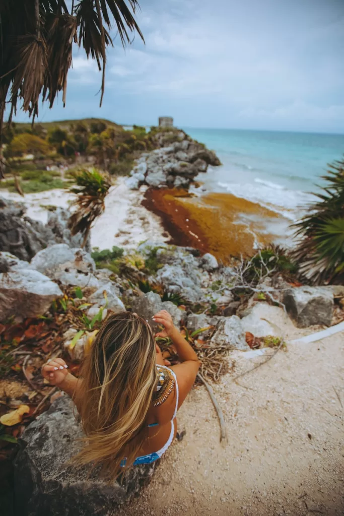 woman sitting on gray rocks near palm trees Mayan Riviera Safe