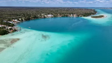 a large body of water with a beach and houses in the background Bacalar Lagoon