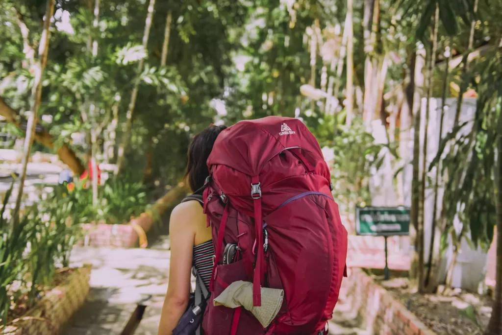 person with red trekker backpack standing on pathway surrounded with tall and green trees during daytime female solo travel to find if cabo san lucas safe