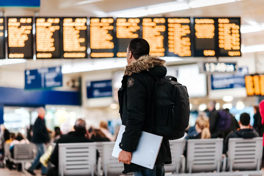 man standing inside airport looking at LED flight schedule bulletin board on how to Purchase Travel Insurance for Mexico