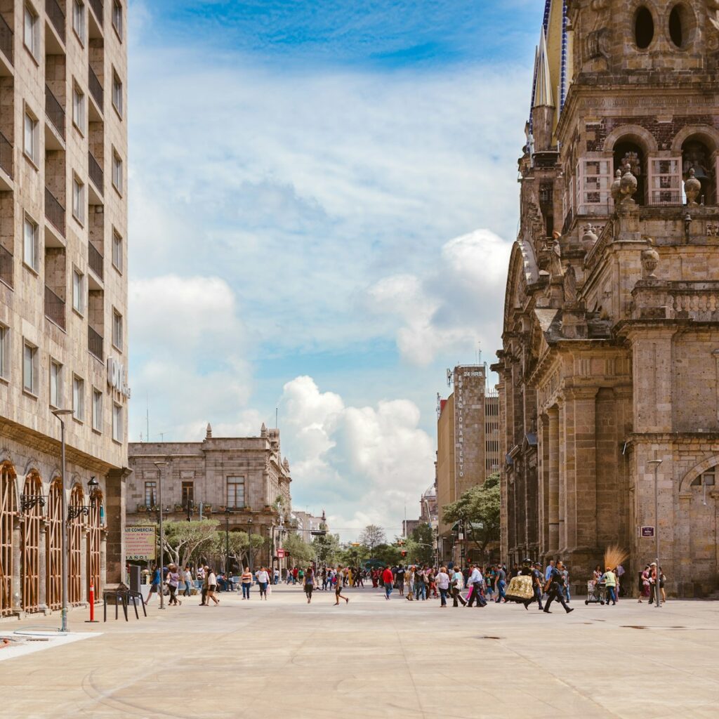 people walking near brown ancient cathedral under white and cloudy skies Guadalajara