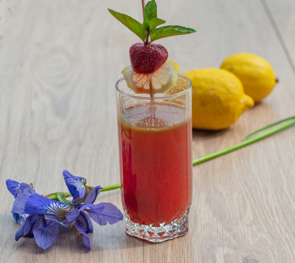 a glass filled with liquid next to lemons and a flower Berry Lemonade