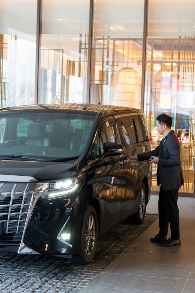 A man in a suit standing next to a black car private driver