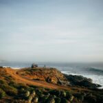 a couple of people standing on top of a hill next to the ocean Eréndira