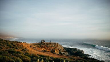 a couple of people standing on top of a hill next to the ocean Eréndira