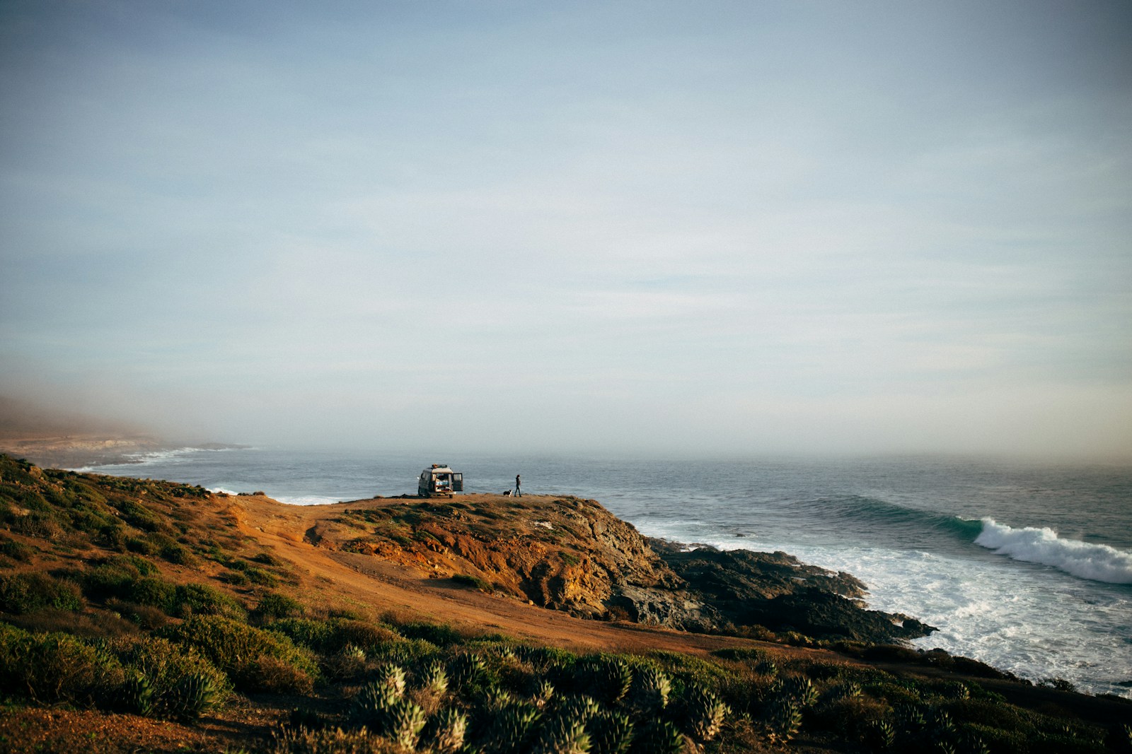 a couple of people standing on top of a hill next to the ocean Eréndira