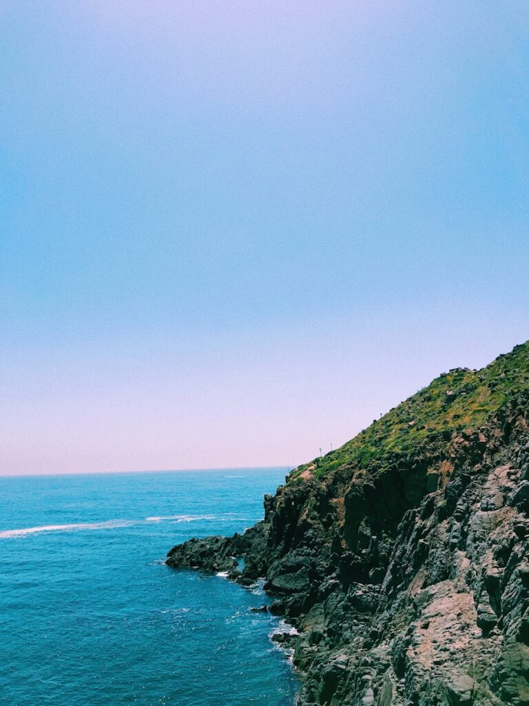 green and brown mountain beside blue sea under blue sky during daytime Bufadora