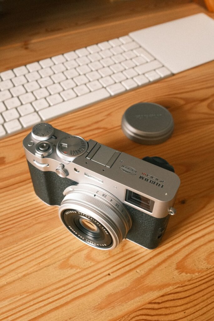 a camera sitting on top of a wooden table next to a keyboard Fujifilm X100VI